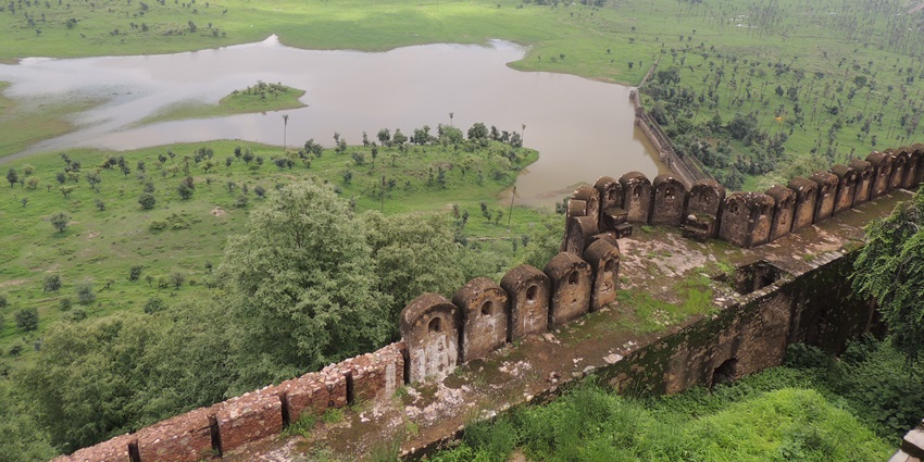 Scenic view of a fort wall overlooking a lush green valley with a river and distant hills.