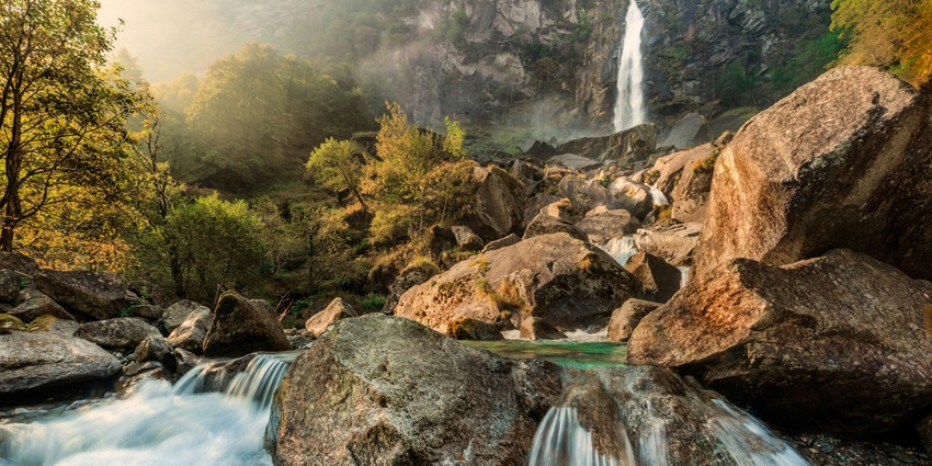 Scenic view of Kapil Dhara Waterfall flowing through rocky terrain surrounded by greenery.