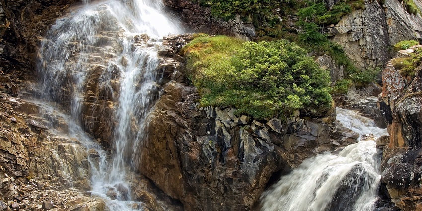 Powerful waterfall flowing over large rocks into a river, surrounded by lush greenery