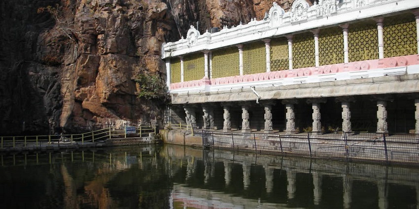 A picture of a wall of a temple with its reflection forming in a pond in front, with a hill in the background