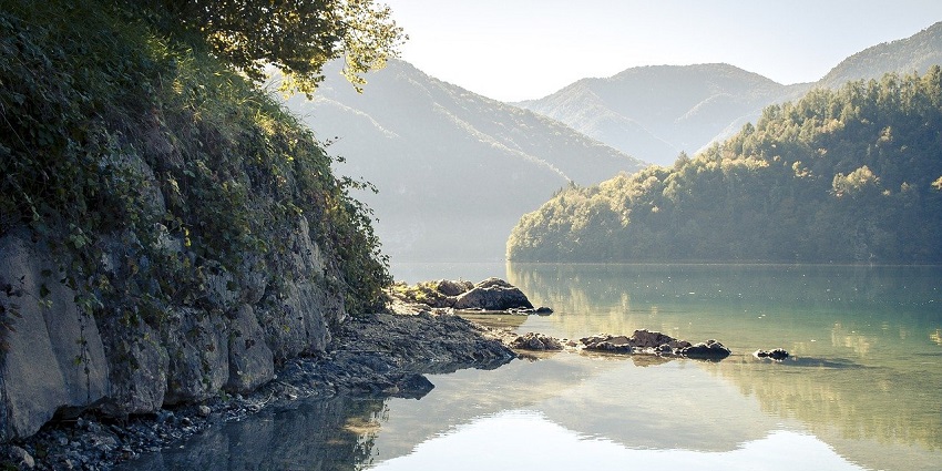 Picturesque view of rocky shore of a lake, reflecting the blue sky in the serene water