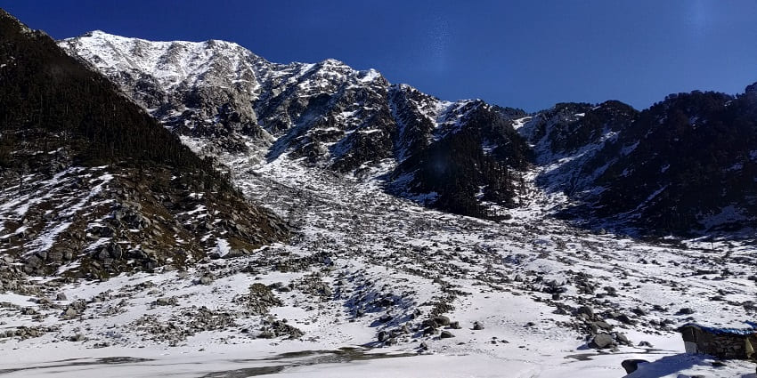 Kareri Lake near Dharamshala, surrounded by rocky terrain and lush greenery under a clear sky