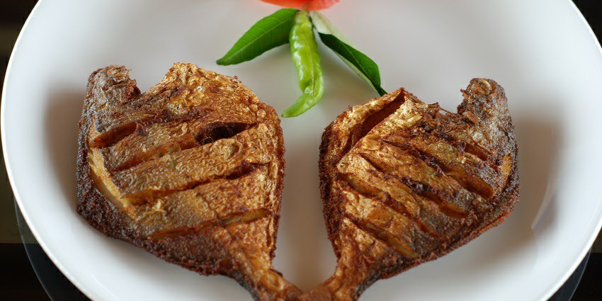 Crispy fried Karimeen fish served on a plate, garnished with lemon and herbs.
