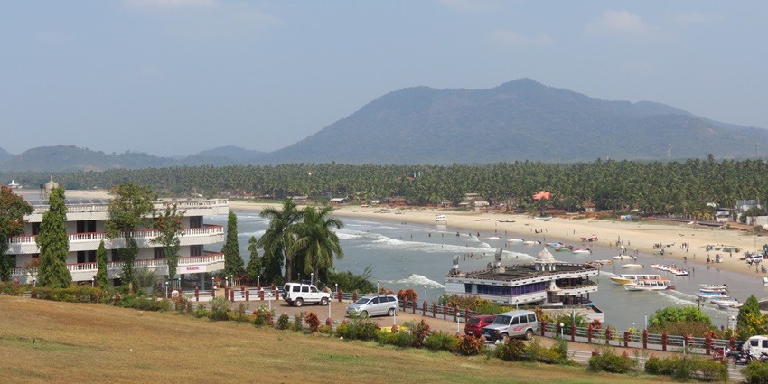 Karwar Beach features a pristine beach, greenery in the background, and traditional boats.