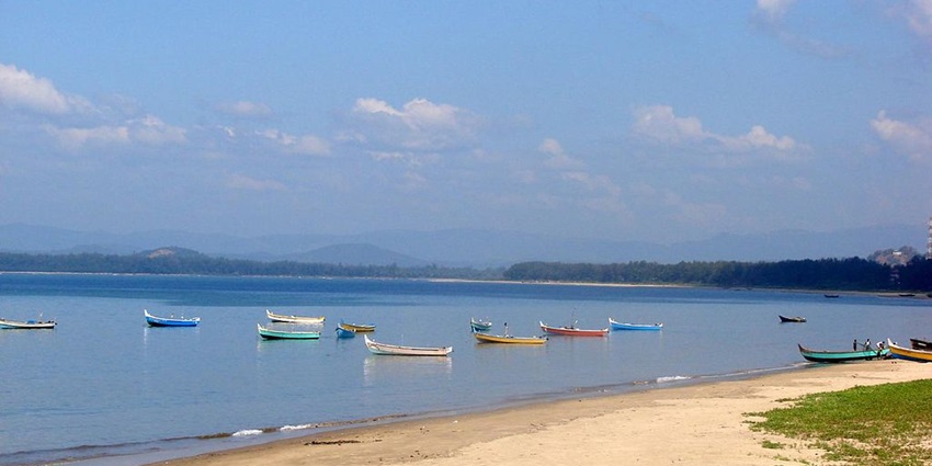 Karwar Beach with golden sands, a backdrop of verdant hills, and fishing boats on the water
