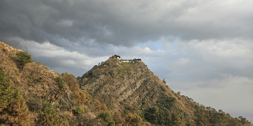 Image of Kasauli hill station with a house on top of the hill under cloudy sky