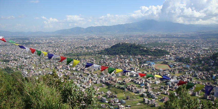 A picture taken from a hilltop of a valley in Nepal with greenery and residential houses spread across