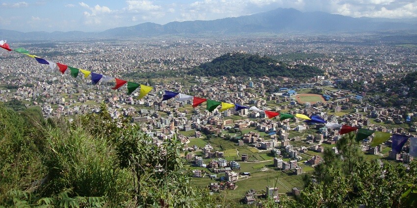 A picture taken from a hilltop of a valley in Nepal with greenery and residential houses spread across