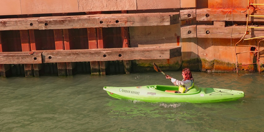 A breathtaking view of a person enjoying kayaking on a green boat on a water body.