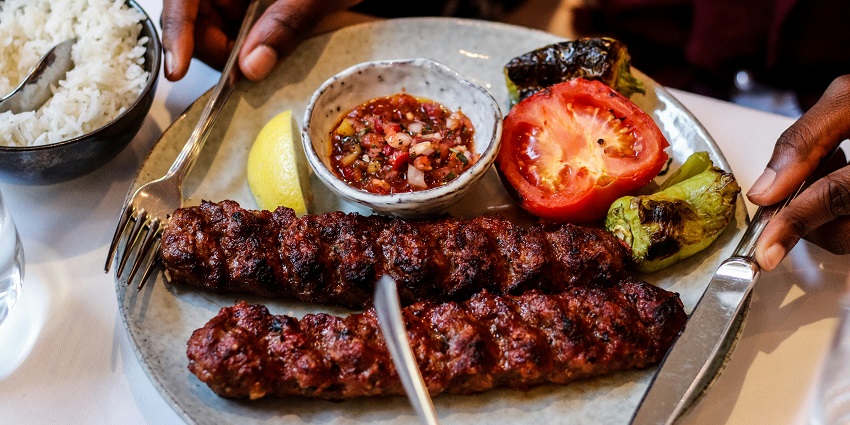 Image of two Kebab served on a white plate with side roasted vegetables like tomatoes