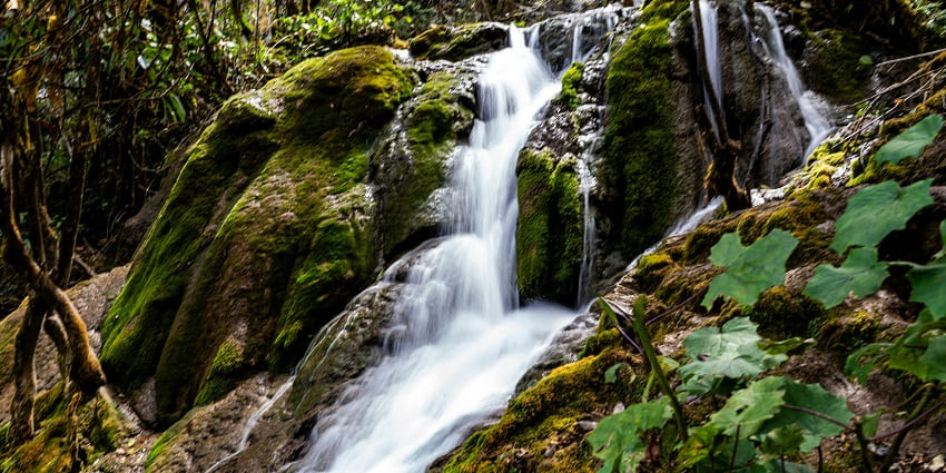 Kemburli Waterfall cascades down rocky cliffs, surrounded by lush greenery
