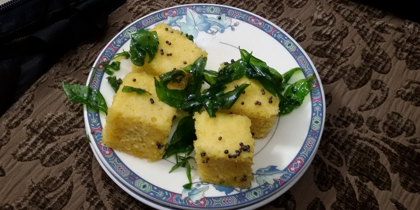 Sweet khaman garnished with curry leaves and green chillies being served on a plate.