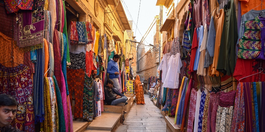 A narrow street with colorful clothes hanging and displaying on all shops