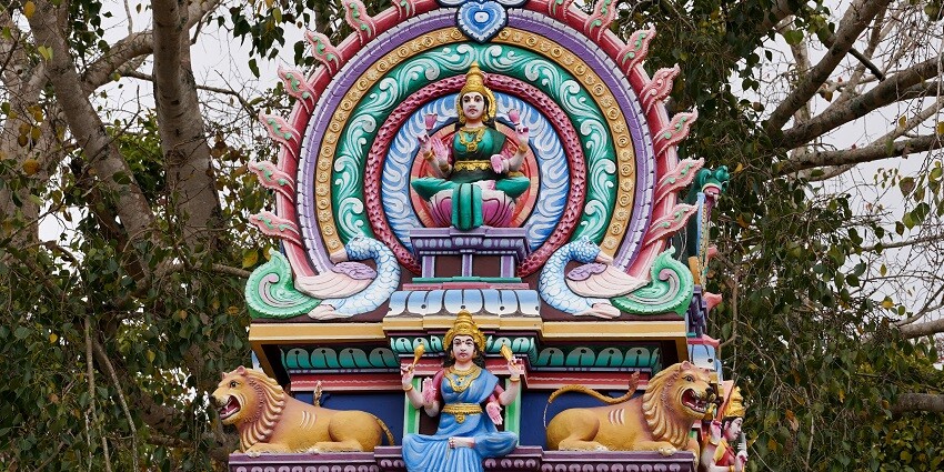 A colourful and vibrant statue of goddess Durga surrounded by lush greenery.