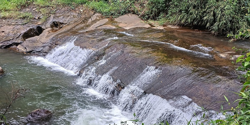 A picture of a quaint waterfall cascading down a rocky terrain, surrounded by greenery