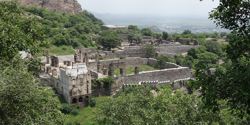 An aerial picture of a fort with traditional architecture and a long wall in front of it, surrounded by greenery