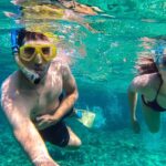 Two people snorkelling underwater exploring marine life capturing themselves in selfie mode.