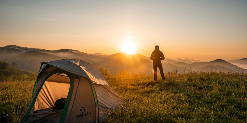 A silhouette of a person standing near a glowing camping tent under a starry night sky, like the best camp in Kufri.