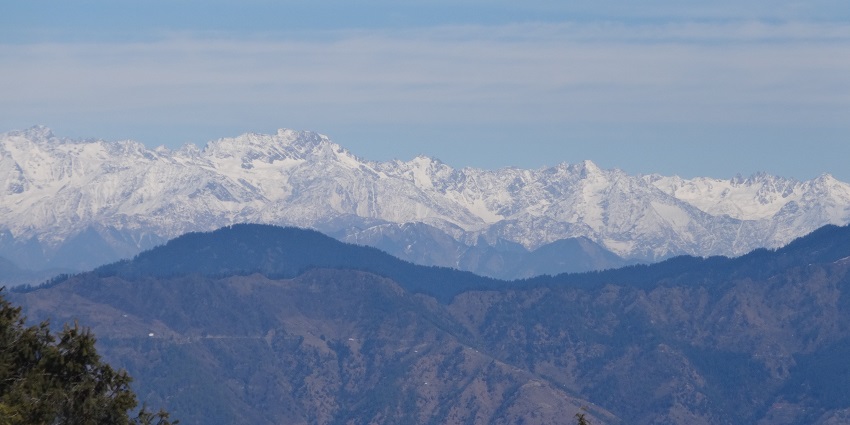 A scenic view of Kufri Hills in Himachal Pradesh, showcasing a lush, verdant landscape with rolling hills and dense pine forests