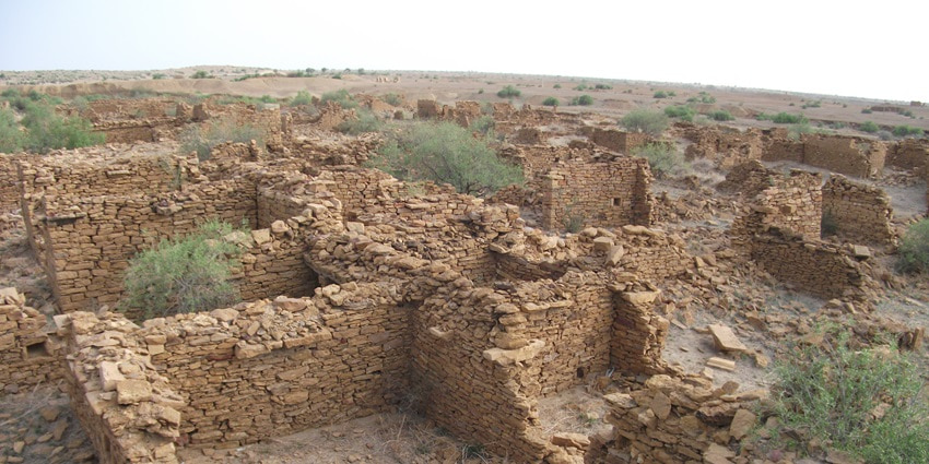Ruins of Kuldhara Village with crumbling stone walls, located in a dry, arid landscape.