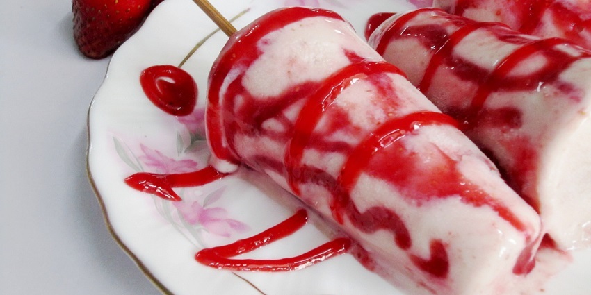 Pink and white strawberry kulfi garnished with raw strawberries and strawberry sauce.