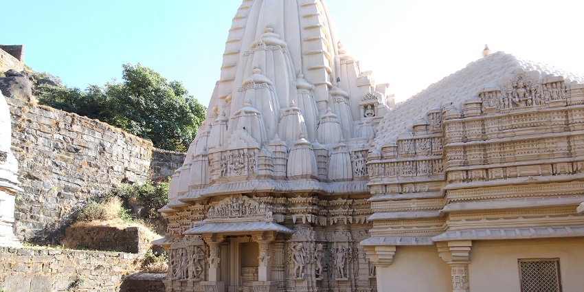 Intricately carved roofs of the Kumar Pal temple with lush trees in the background