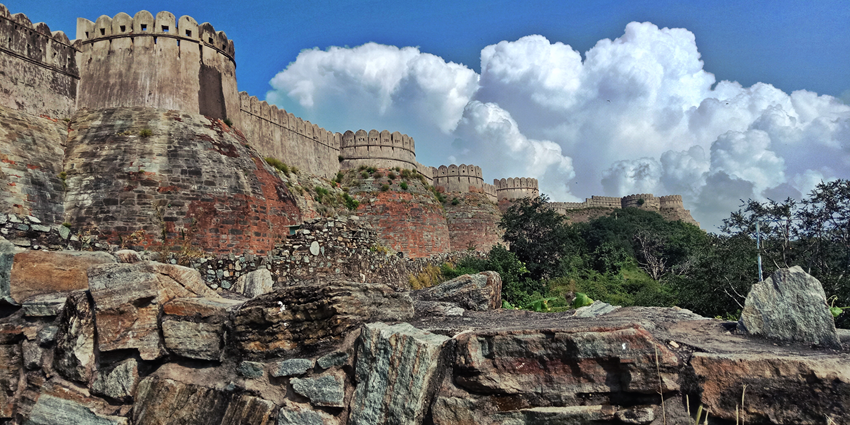 Aerial view of Kumbhalgarh Fort’s massive stone walls winding over the Aravalli hills, with forested valleys stretching into the distance.
