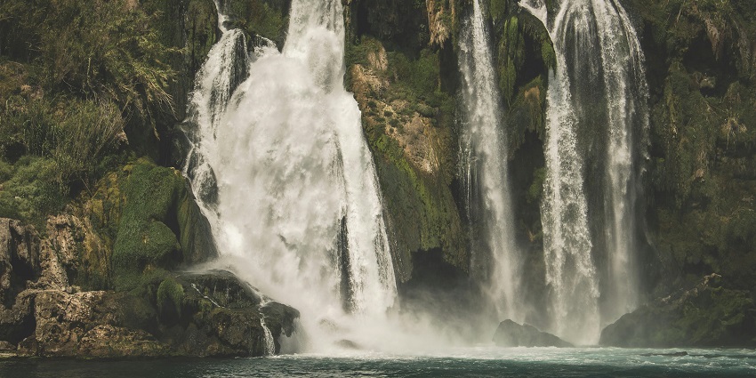 A serene view of cascading white and green waterfalls surrounded by lush greenery