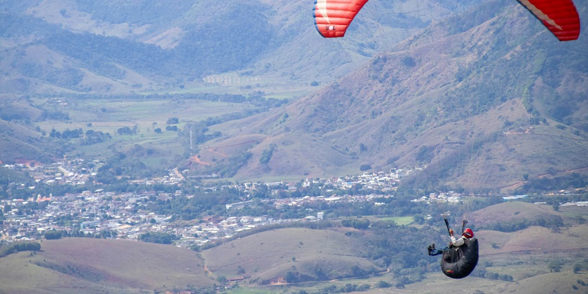 A person paragliding over a scenic valley with a city skyline visible in the background