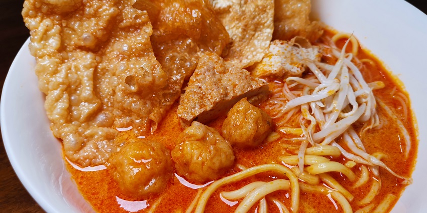 A bowl of traditional laksa with noodles, prawns, and a creamy, spicy coconut broth.