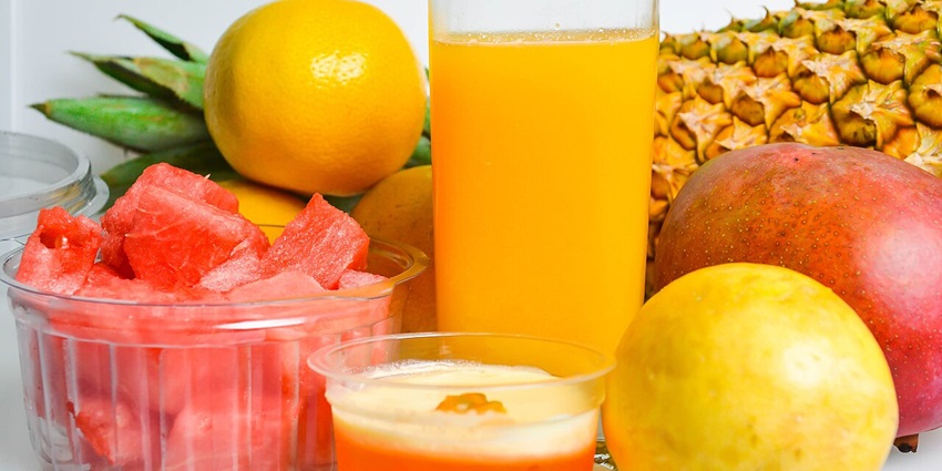 Glass of golden pineapple juice surrounded by fresh pineapple, orange, watermelon slices