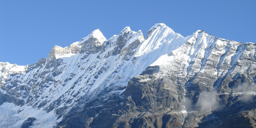 The scene showcases a stunning contrast between the rugged, snow-capped peaks and the lush green valley below