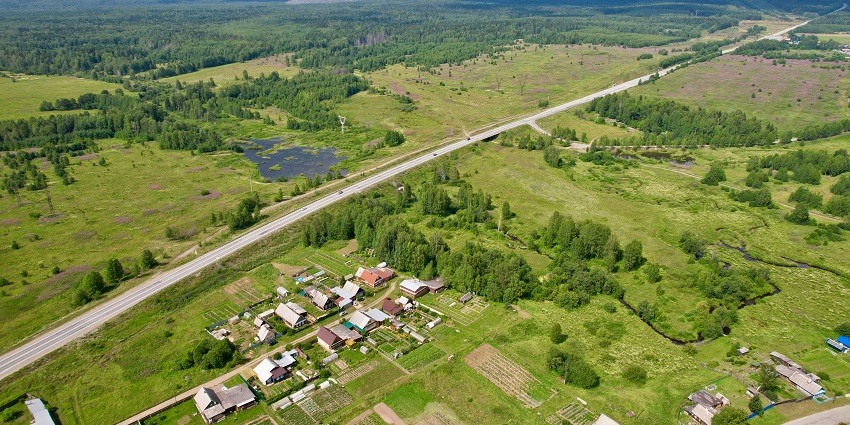 A scenic view of a traditional village surrounded by forested mountains under a clear sky.