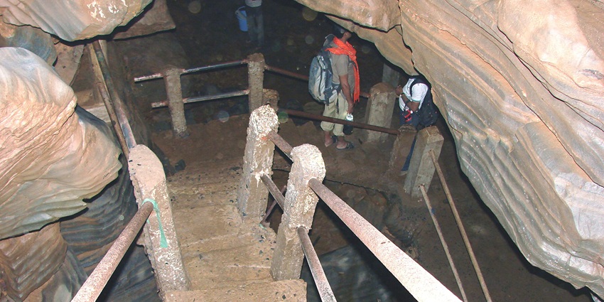People going down the concrete pathway lead them inside the Kutumsar Caves for exploration.