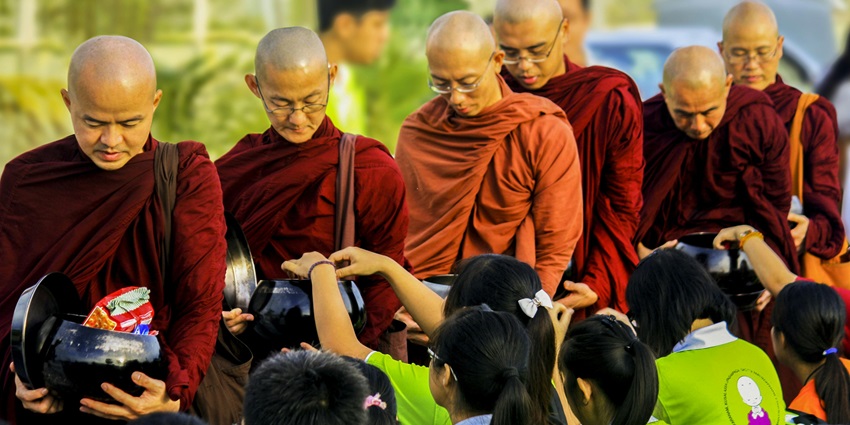 Image of buddhist monks walking in line and receiving food from school kids