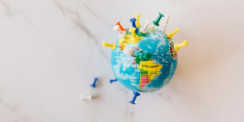 A selectively focused view of a colourful globe with assorted push pins on it on a table.