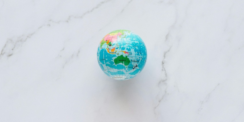An aerial shot of a blue and green globe sitting on a plain white surface during the day.