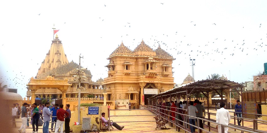 People are positioned outside the Somanath temple, surrounded by birds in flight.