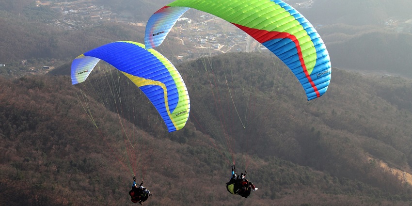 A stunning view of two people paragliding over lush green terrains during the daytime.