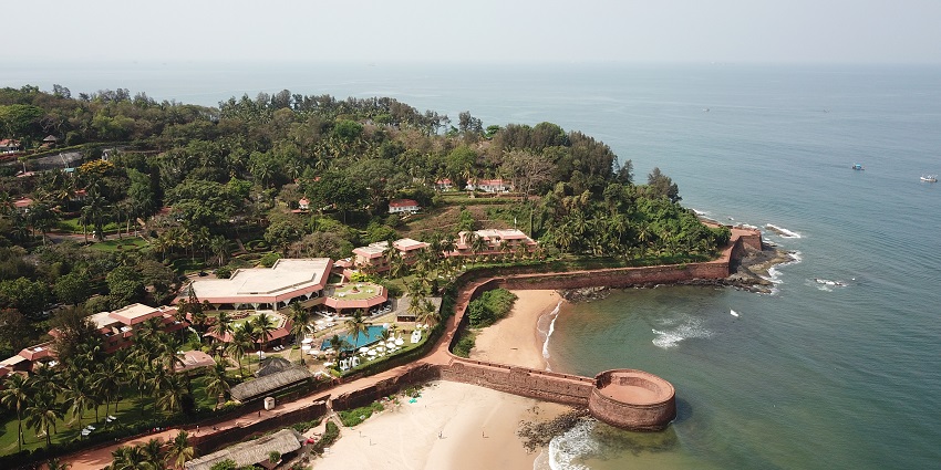 Aerial view of Goa resorts and hotels near the beach under clear blue sky and palm trees around