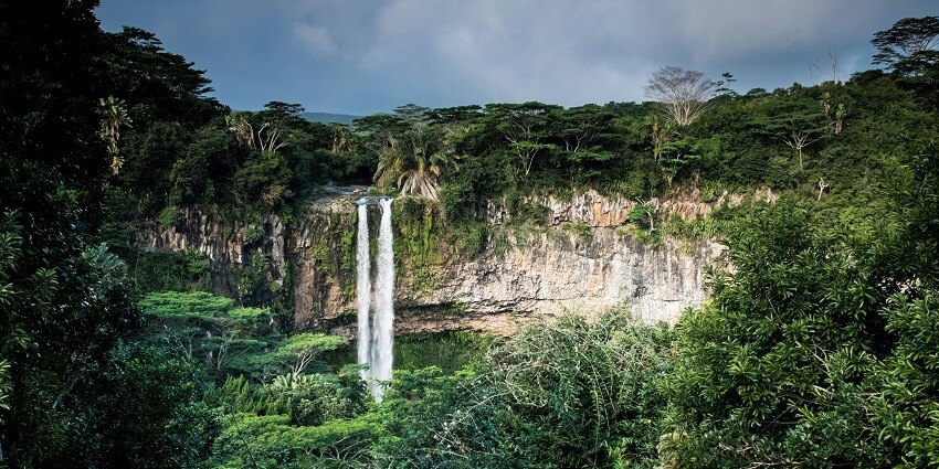 A serene waterfall cascades down rocky cliffs, surrounded by lush green trees