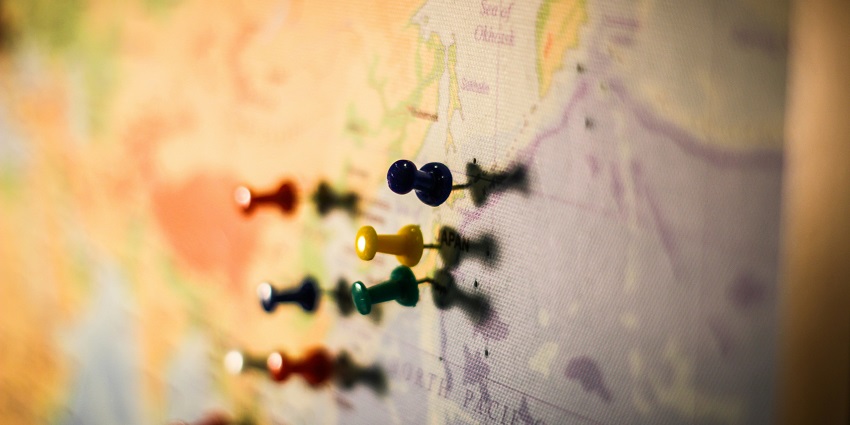A stunning view of a colourful world map with assorted push pins in it on a wall.