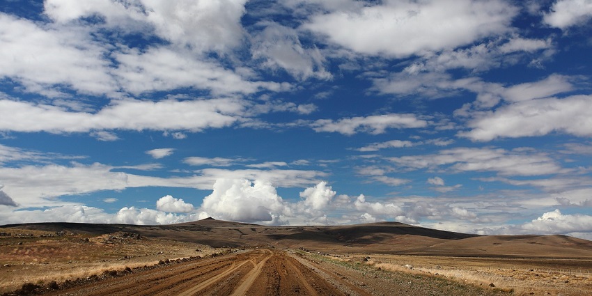 An empty road with low mountains in front. The sky is filled with clear clouds.
