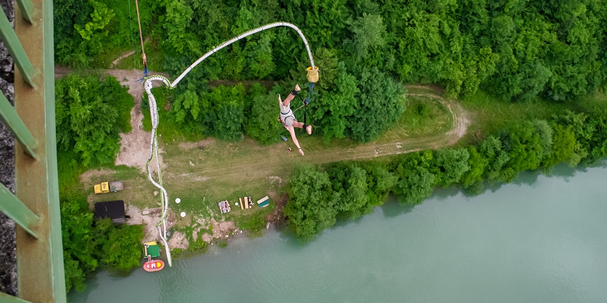 Image of a man bungee jumping from top with aerial view of lush greenery and water
