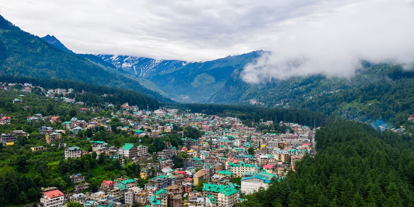 An aerial view of Manali with its hotel buildings and houses under a clear, bright blue sky.