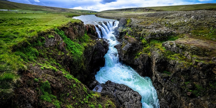 A picture of a waterfall slowly cascading down, surrounded by a green field