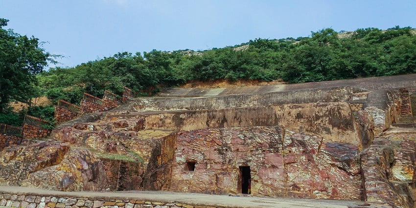 A view of Sonbhandar Caves showcasing ancient architecture surrounded by lush green trees.