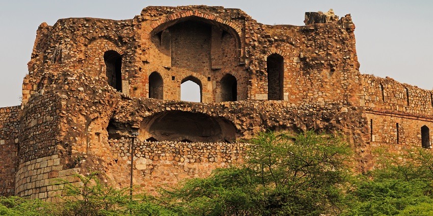 A picture of the ruins of a fort in Delhi with hollow brick walls visible around green surroundings