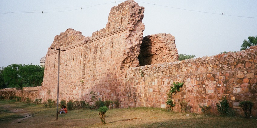 A picture of the ruins of the walls of a fort in Delhi with a sandy area surrounding it