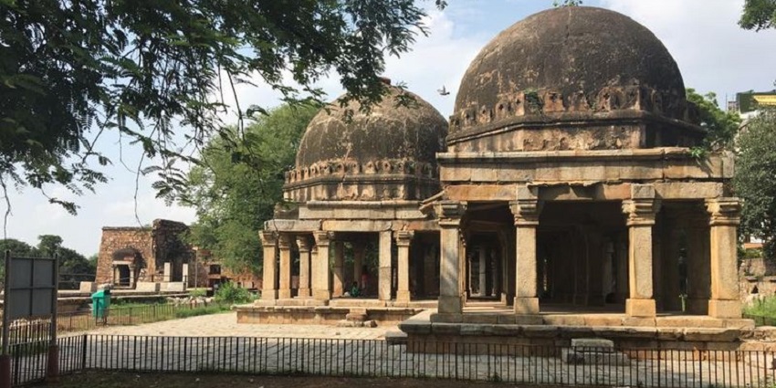 A picture of the Hauz Khas Fort in Delhi taken from a garden area nearby with a dog resting under shade